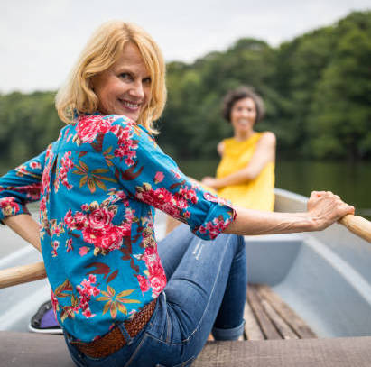 Portrait of smiling mature woman rowing boat in lake. Active female is enjoying boating with friend on vacation. She is wearing casuals.